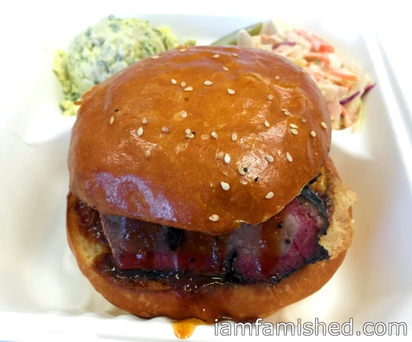 Beef brisket burger with house made crisp apple slaw, potato salad, bbq sauce and a pickle (side view)